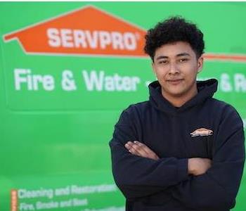 Young, clean-shaven man with mid-length, dark, curly hair wearing a black SERVPRO hoodie, standing next to a SERVPRO truck