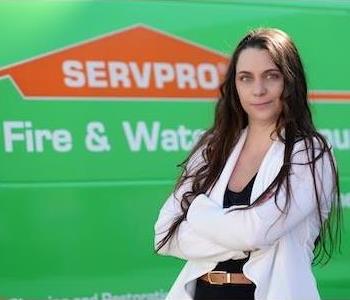 Tall, thin woman with long dark hair and green eyes wearing a white sweater and a slight smile by a SERPRO truck