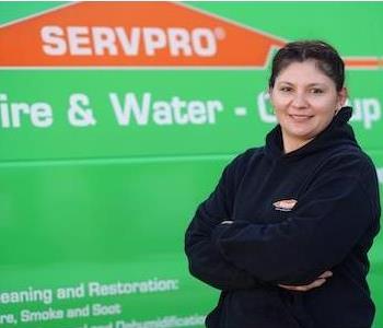 Younger woman with dark hair pulled back wearing a black SERVPRO fleece and a pretty smile standing next to a SERVPRO truck