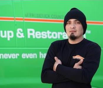 Younger man with a slight beard wearing a black watch cap and long-sleeved SERVPRO shirt, by a SERVPRO truck